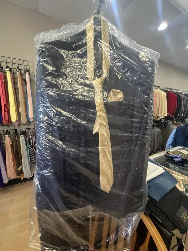 A finished navy suit in a garment bag with a tie, ready for pick-up at Suit Zone